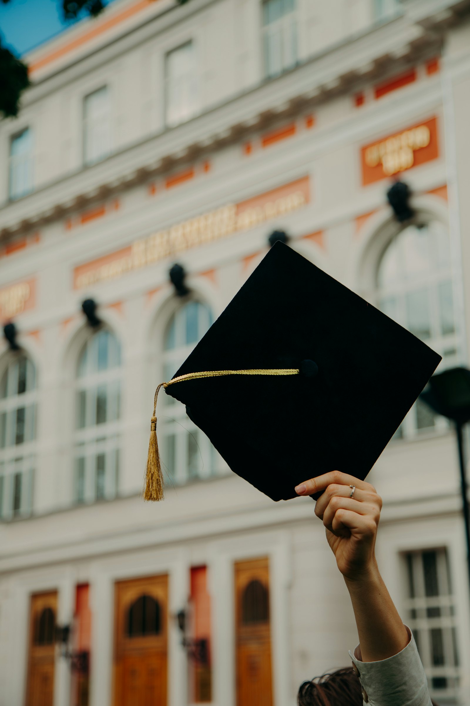 A hand holding up a graduation cap with a gold tassel.