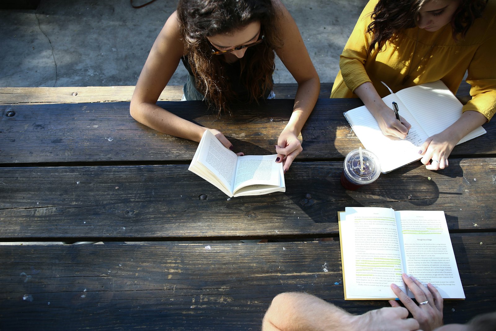 Two people reading books and writing in a notebook at a wooden table.