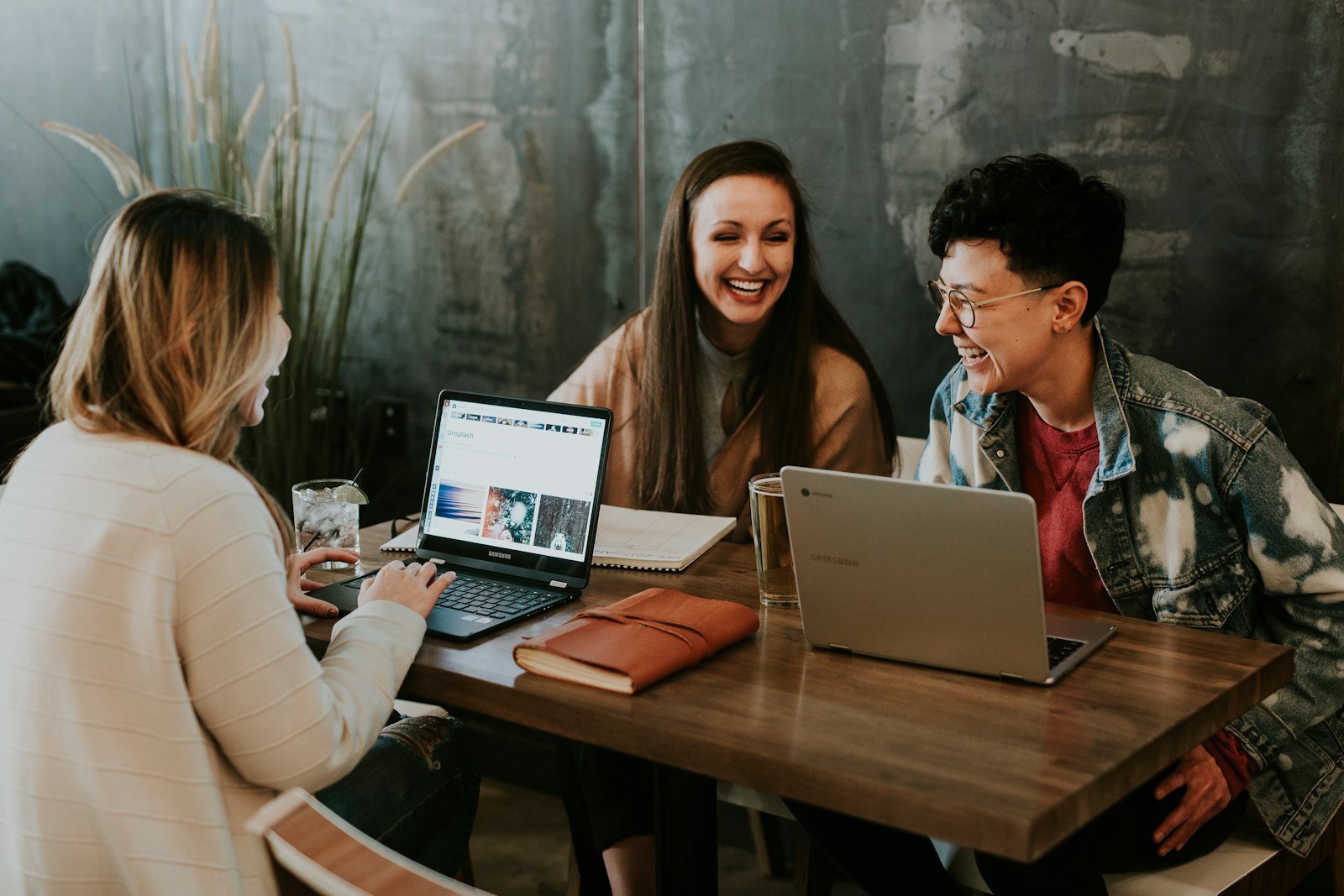 Three people laughing around laptops at a shared table.